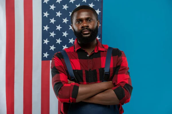 身穿法兰绒工作服和工作服 头戴长胡子的年轻非洲裔美国人 靠着星条旗的背景 手挽手站在胸前 — 图库照片