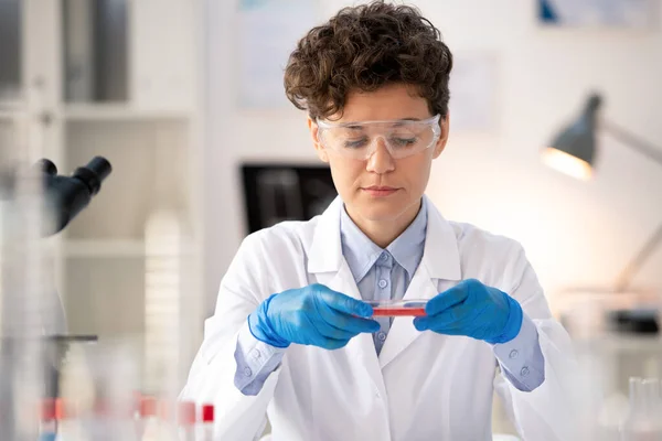 手袋の現代女性科学者は 研究室の職場に座って 小さなフラスコで血液のサンプルを扱う — ストック写真