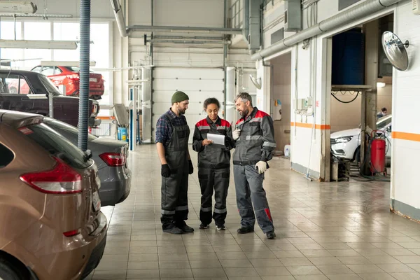 自動車整備センターの3人の異文化間労働者が自動車のワークショップに立ち いくつかの技術的な質問について議論する — ストック写真