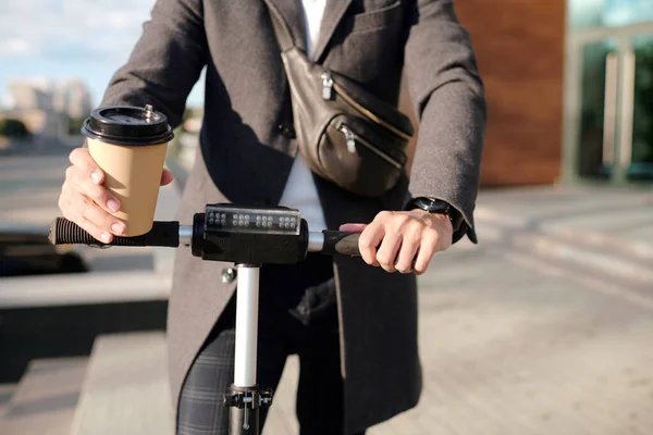 都市部の環境でコーヒーのガラスを保持し 電動スクーターに乗ってコートでエレガントなビジネスマンの手仕事を急いでいる間 — ストック写真