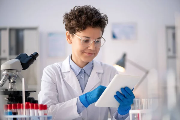 オンライン情報を通して見る手袋 ホワイトコート 眼鏡の幸せな若い現代女性科学者や薬剤師 — ストック写真