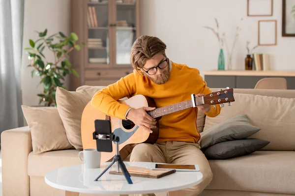 Telli müzik aleti olan sakallı genç bir müzisyen çalmadan önce müzik veya akustik gitar çalıyor.