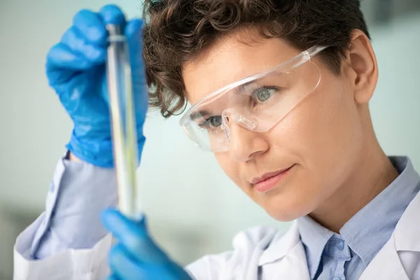 科学实验室调查期间 戴手套 眼镜和白色眼睛的年轻女研究员研究瓶子中的物质 — 图库照片