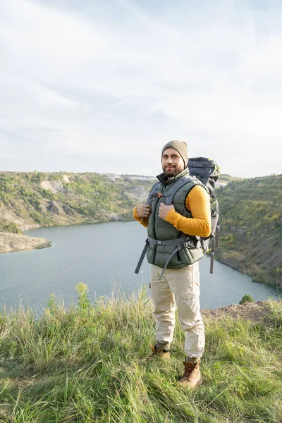Szczęśliwy Młody Brodaty Turysta Plecakiem Stojącym Szczycie Góry Nad Jeziorem — Zdjęcie stockowe