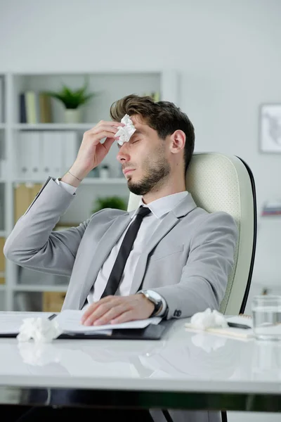オフィス 風邪やインフルエンザの概念で紙で作業しながら デスクに座って鼻水をこすり若いビジネスマンが病気 — ストック写真