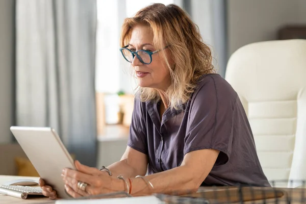 Rijpere Zakenvrouw Casualwear Bril Kijken Naar Tablet Display Terwijl Zitten — Stockfoto