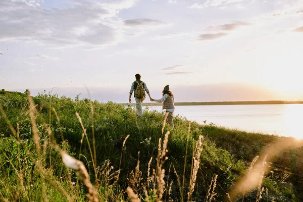 年轻男子在日落时牵着女友的手一起登山的后视镜 — 图库照片
