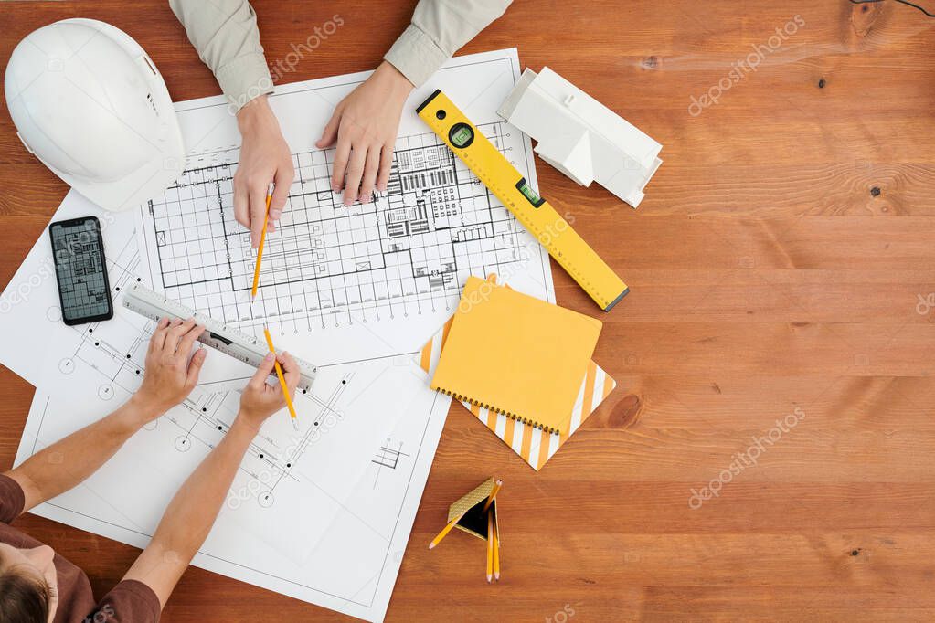 Top view of hands of two contemporary engineers or architects discussing sketch of new building project surrounded by working supplies