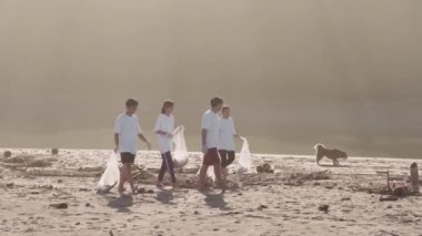 Çevre topluluğunun dört üyesinin çöpleri topladıktan ve evsiz köpekleri takip ettikten sonra sahil boyunca çöp torbalarıyla yürüdüklerinin tam bir yan görüntüsü.