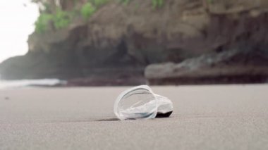 Dikkatsiz bir insan tarafından kıyı şeridine atılan buruşmamış tek bir plastik bardağa yakın çekim.