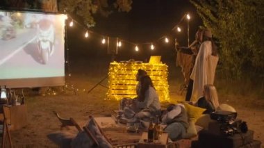 Arkadaşlarla boş zamanlarını açık havada film izleyerek geçiriyorlar. Parlak sicim ışıkları ve sinema ekranı olan rahat bir yerde yiyip içiyorlar.