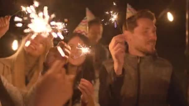 在夏天的夜晚 戴着派对帽的快乐的朋友们在户外庆祝生日 在户外点燃火花 一起玩乐 — 图库视频影像