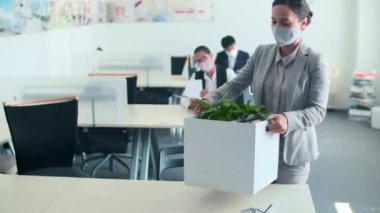 Yüzüne koruyucu maske takan tanınmayan bir kadın işe geri dönüyor ve eşyalarını kutusundan çıkarıyor.