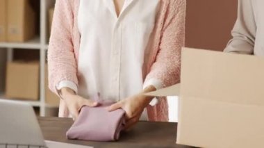 Online mağaza siparişlerini paketlerken tanınmayan kadınların katlama ve karton kutuya koymalarının orta bölüm izleme görüntüsü.