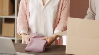 Katlanmış giysileri karton kutuya koyup, müşterilerin siparişlerini hazırlarken bantla mühürleyen çok ırklı genç kadınların çekimleri.