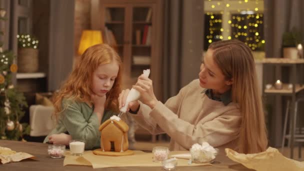 年轻快乐的女人和她那可爱的小女儿在圣诞桌上用奶油装饰姜饼屋的一系列镜头 — 图库视频影像