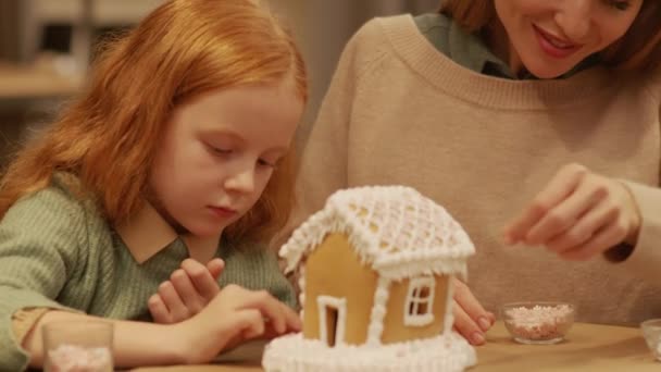 若いですCaucasian女性飾る大きなジンジャーブレッドハウスとともに小さな雪の結晶とともに小さな娘取得準備クリスマスお祝い — ストック動画