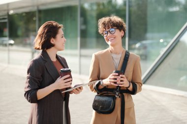 İki neşeli bayan meslektaşı içki içerek şehir ortamında konuşuyor ve gülüyor iş merkezinin önünde dikiliyorlar.