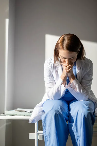 화이트 코트와 파란색 제복을 의료용 손수레에 누군가를 위해기도 데지친 간호사 — 스톡 사진