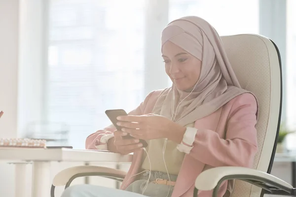 Jonge Glimlachende Moslim Zakenvrouw Hijab Scrollen Smartphone Terwijl Zitten Fauteuil — Stockfoto