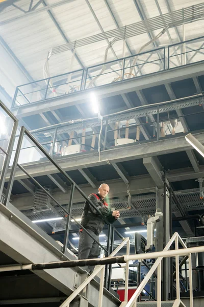 階段の前に現代的な大規模なポリマー加工工場内に立つ作業着のバルド成熟したエンジニアやフォアマン — ストック写真