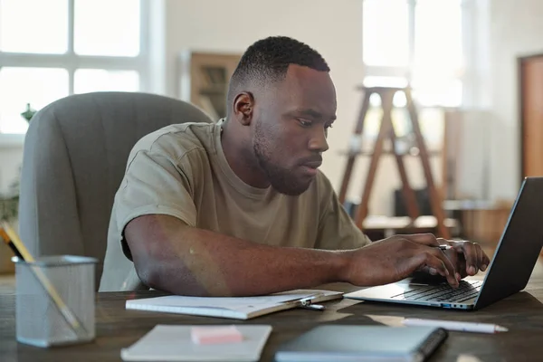 在客厅浏览在线数据时 非洲年轻男性自由职业者或家庭办公室经理在笔记本电脑前按桌子打字 — 图库照片