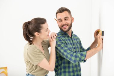 Heyecanlı genç sakallı adam merdivende dikiliyor ve duvara vida örüyor.