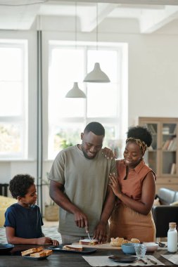 Genç Afrikalı adam kahvaltıya sandviç hazırlarken sevgi dolu karısı ve onun sevimli küçük oğlu için ekmek kesiyor.