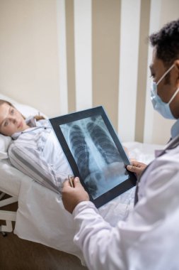 Erkek radyologlar, hastane odasında yatağında yatarken kadın hastaların röntgen görüntülerine bakıyor.