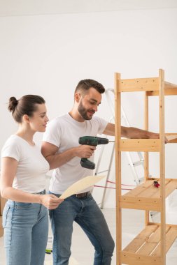 Hoşnut genç bir kadın yeni bir dairede mobilya montajında kocasına yardım ederken okuma dersleri alıyor.