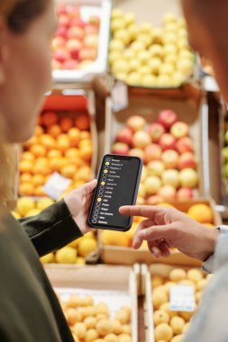 Çiftçi pazarından yiyecek alırken akıllı telefondan ürün listesini kontrol eden genç çiftin omuz manzarası üzerinden