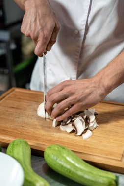 Modern restoranın genç erkek aşçısının elleri lezzetli yemekler pişirirken tahta tahtada taze şampiyonlar kesiyor.