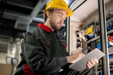 Çağdaş, genç, ciddi iş kıyafetleri mühendisi ve touchpad 'deki teknik verileri tarayan bir endüstriyel makine.