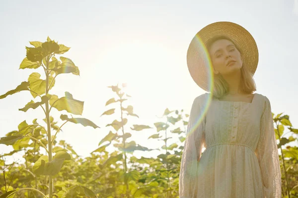 美丽的年轻女子 戴着草帽 身穿白色乡村风格的衣服 在夕阳西下站在相机前看着你 — 图库照片