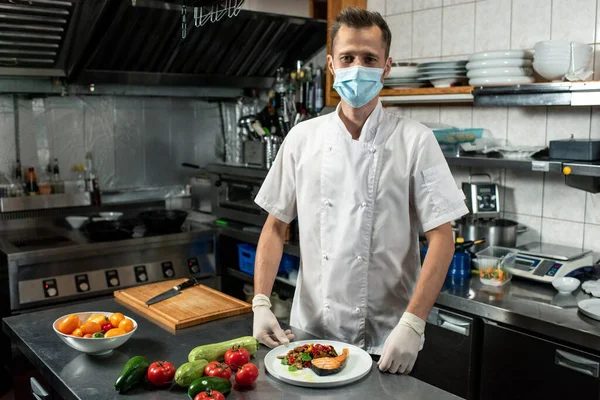 白を基調としたプロの料理人で 揚げ鮭を皿の上に盛り付け 台所で野菜を蒸したもの — ストック写真