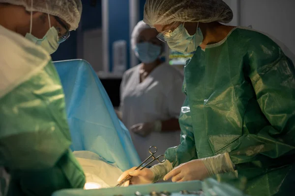 两名穿着工作服 戴防护面具 戴眼镜和手套的专业外科医生在手术期间弯腰对着病人的助手 — 图库照片