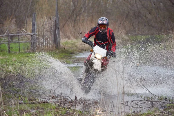 Motorcross rider racing in flooded wood and splashing dirty water of puddle