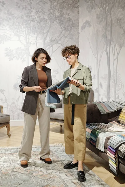 两名年轻的当代女性室内设计师站在工作室里 在选择新家具用纺织品样品时进行咨询 — 图库照片