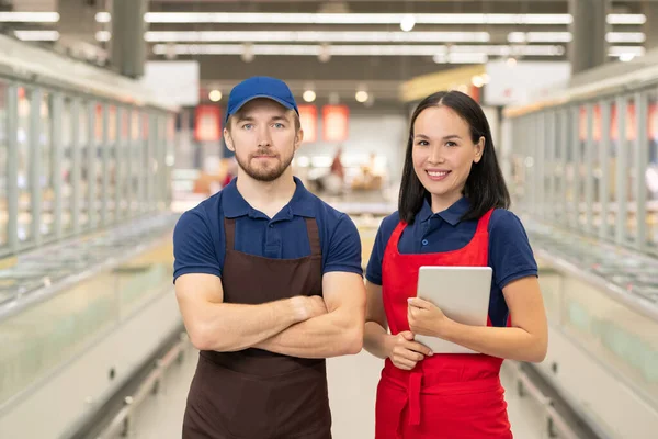 Yatay orta boy portre. Eğer erkek ve kadın üniforma giyerse. Süpermarket koridorunda yan yana durup kameraya bakarlar.