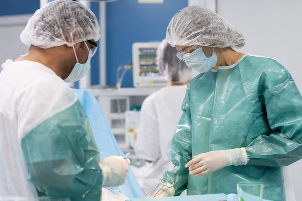 两名专业外科医生在操作时弯腰保护病人 并由医疗设备辅助站在旁边 — 图库照片