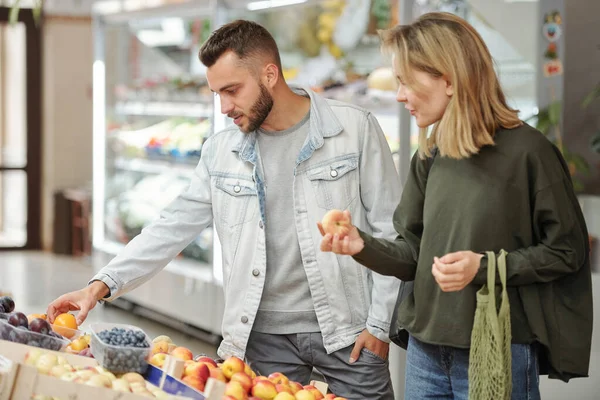 身着休闲装的年轻夫妇站在食品柜台前 在农贸市场上寻找成熟的水果 — 图库照片