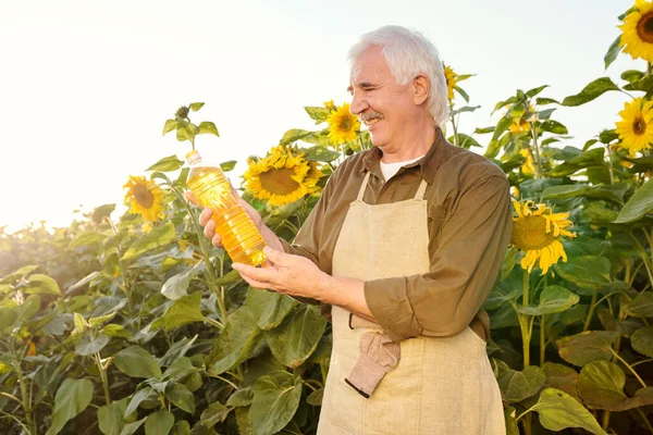 Samtida Senior Gråhårig Man Förkläde Och Skjorta Tittar Flaska Solrosolja — Stockfoto