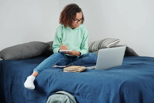 Молода Студентка Змішаної Раси Сидить Ліжку Перед Ноутбуком Робить Нотатки — стокове фото
