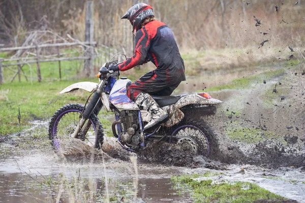 Motorcross rider racing in dirt track while moving in deep puddle