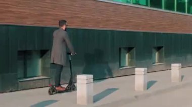 Şık giyinmiş modern yakışıklı adamın şehirde elektrikli scooter sürerken tam bir arka plan çekimi.