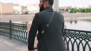 Şehir merkezinde nehir ve modern müze binası olan ve arka planda elektrikli scooter kullanan yetişkin bir adamın yukarı aşağı görüntüleri.