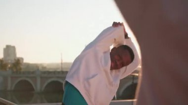 Beyaz kapüşonlu genç adamın orta boy fotoğrafı. Şafak vakti şehir merkezinde, kadın partnerle birlikte yan büküş yaparken.