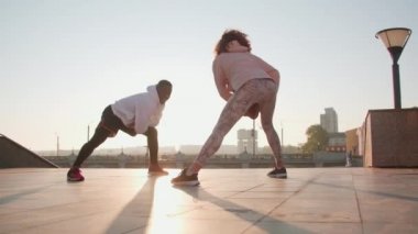 Ağır çekimde gülümseyen Afro-Amerikan sporcusunun sabah güneş ışığında kadın partneriyle dışarıda çalışırken.
