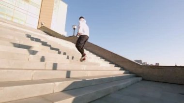 Gündüz vakti şehir merkezindeki uzun cam binanın merdivenlerinde koşup duran sağlıklı erkek Afrikalı Amerikalı koşucu.