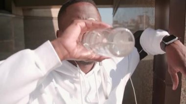 Yakışıklı Afro-Amerikan koşucu, kulaklık takmış ve açık havada koşu yaptıktan sonra spor şişesinden su içmiş.